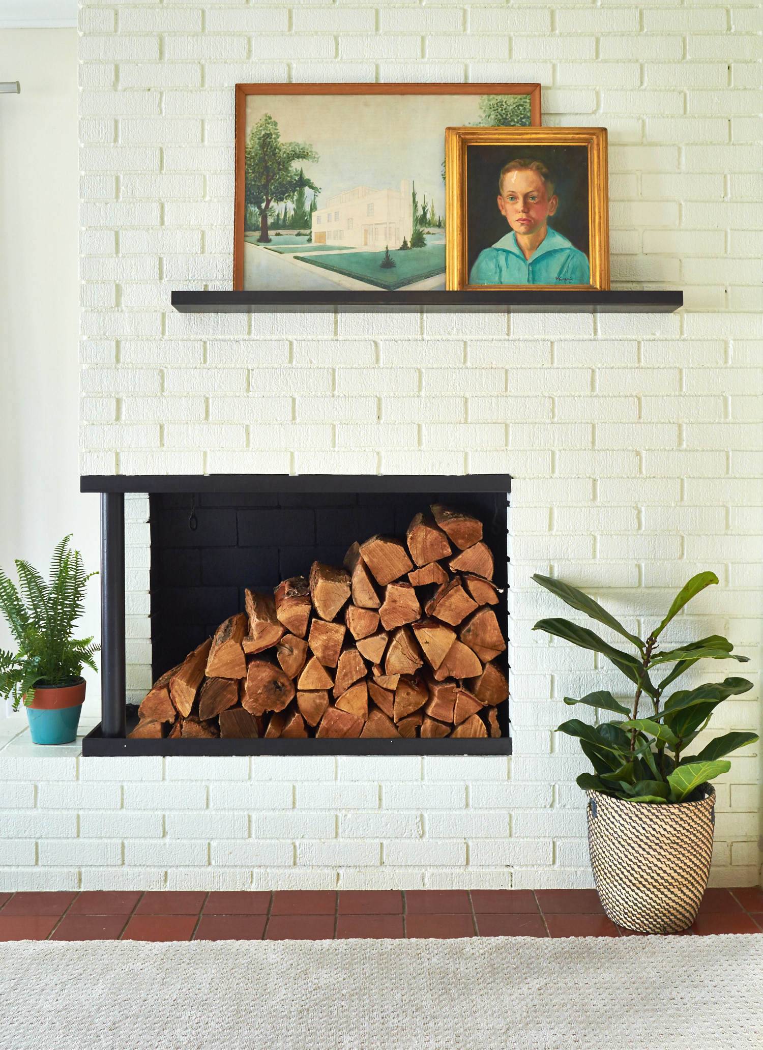 Fireplace built inside a brick wall with a wood shelf above that holds two framed pictures.