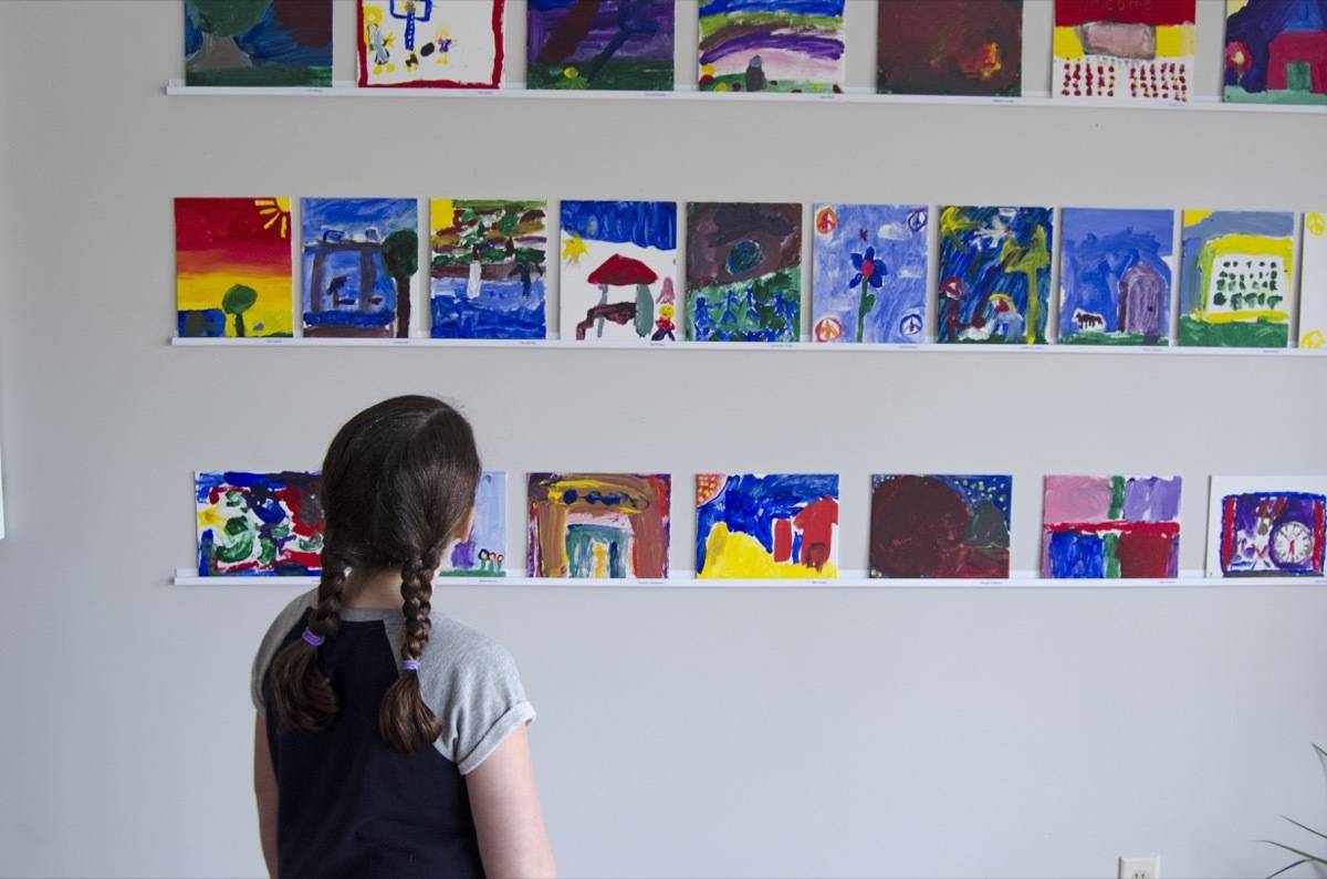 A young girl looking at series of pictures made by little kids stuck up on a white wall