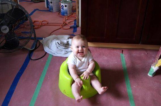 Smiling baby sits in a chair on the floor of a room that is being reconstructed.
