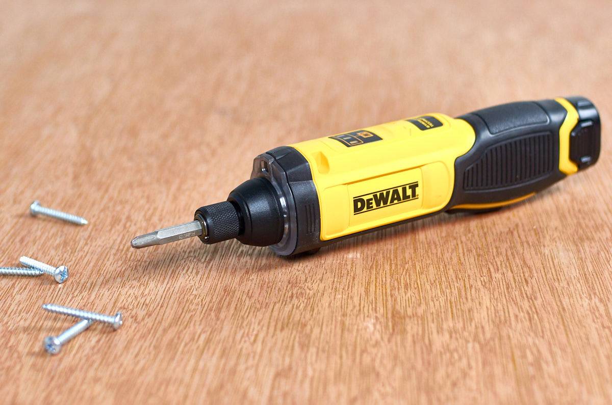 Dewalt electric screwdriver with screws resting on a wood surface.