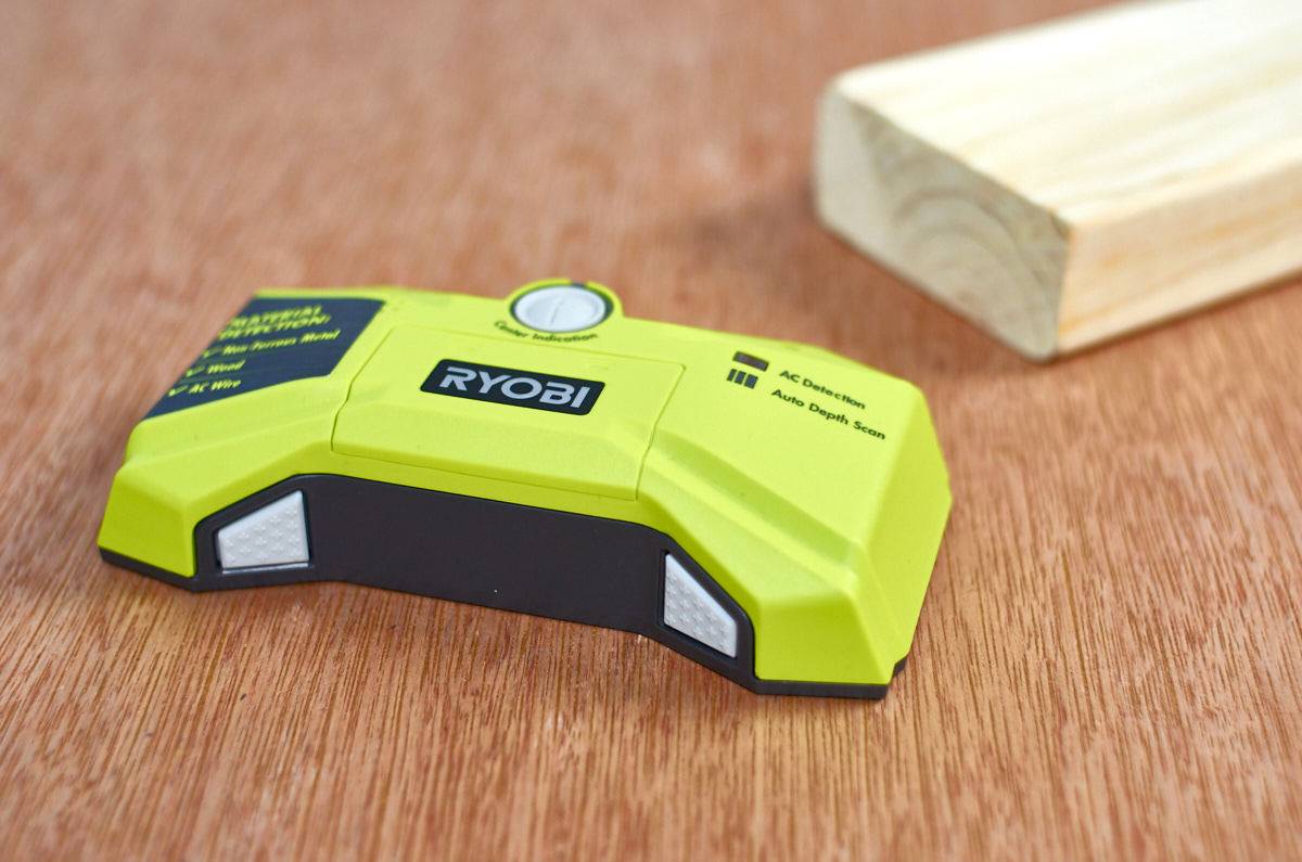 Electronic stud finder next to block of wood.