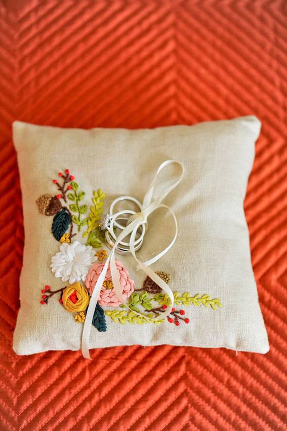 Strands of fiber atop square offwhite pillow with needlework design, set on orange background.