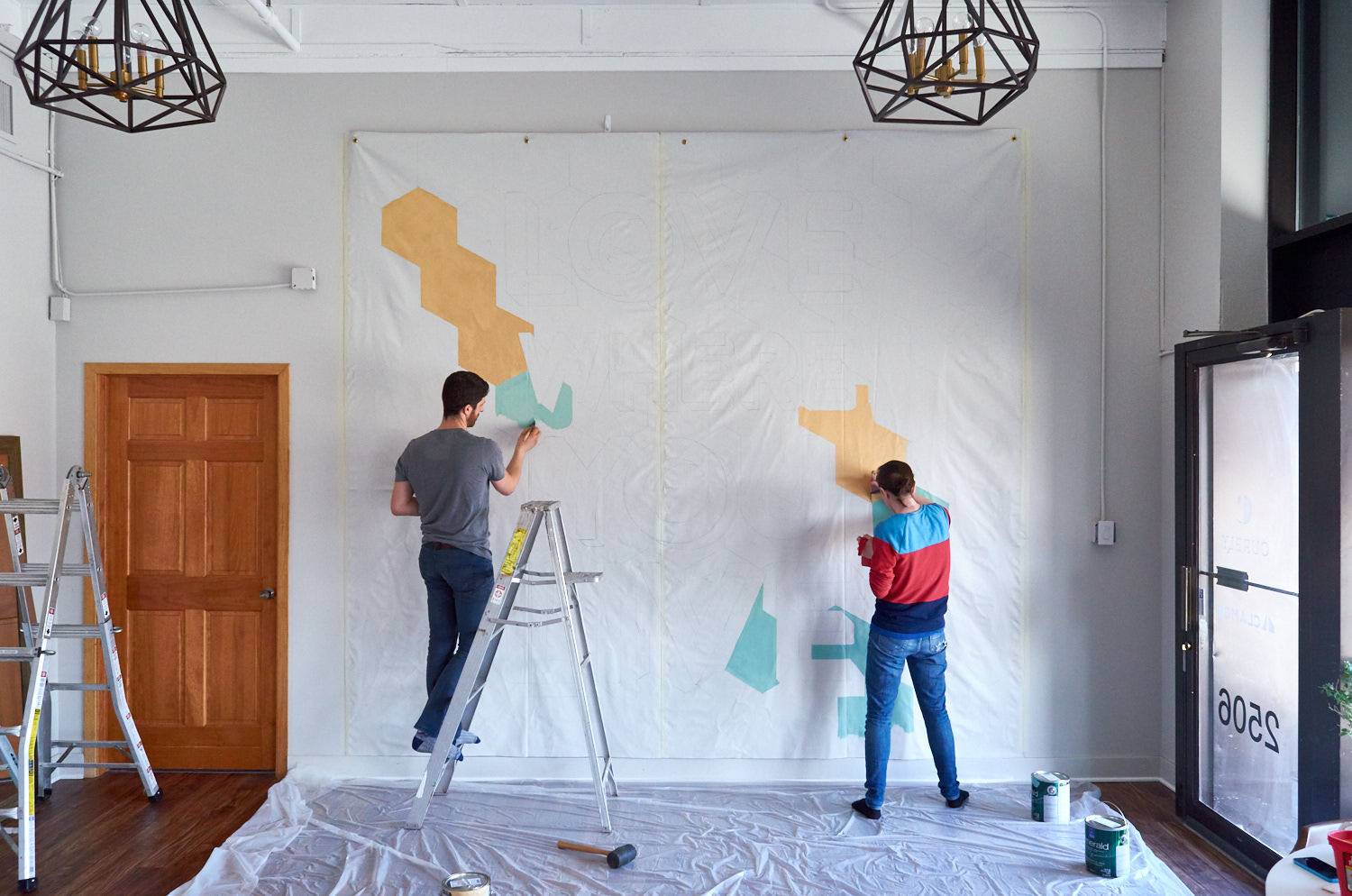 Two people are painting designs to the wall inside the house.