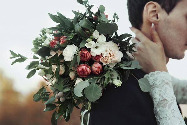 A wedding boquet of flowers against a groom's back.