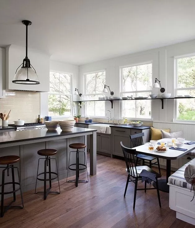 This indoor kitchen and dining area has a small white table with black chairs, as well as bar stools pushed against a counter with a pendant light above.