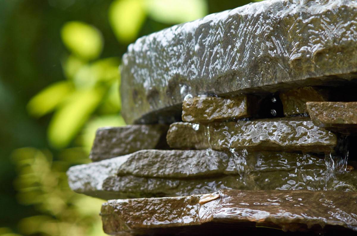 Flat rocks stacked on each other with water pouring down in front of a plant.