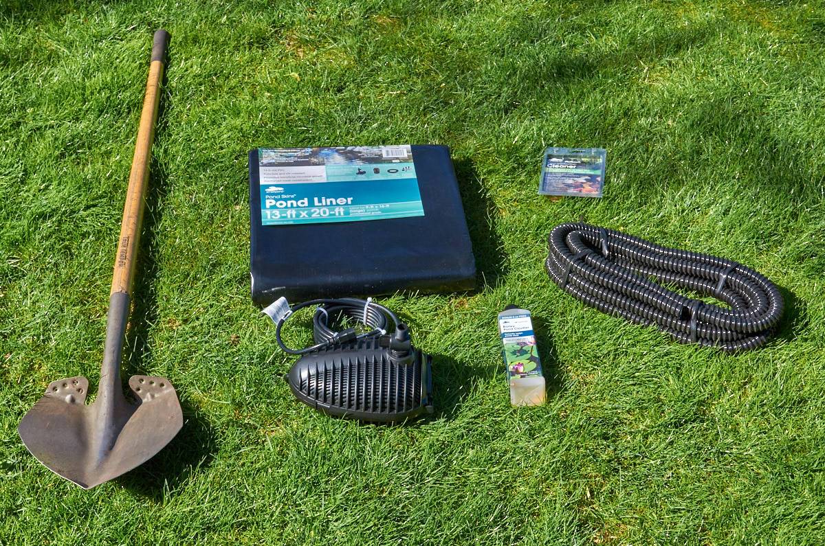 A shovel and other tools sit on the green grass.