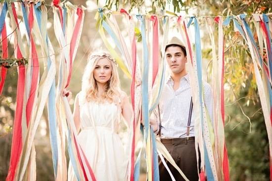 Two people walk through vertically hanging streamers at an outdoor event.