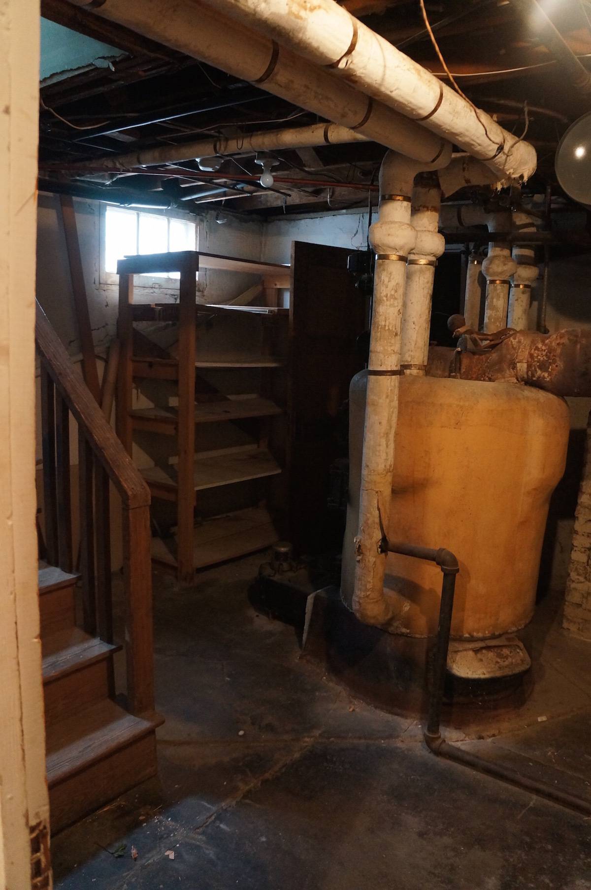 A boiler with ceiling pipes in a basement.