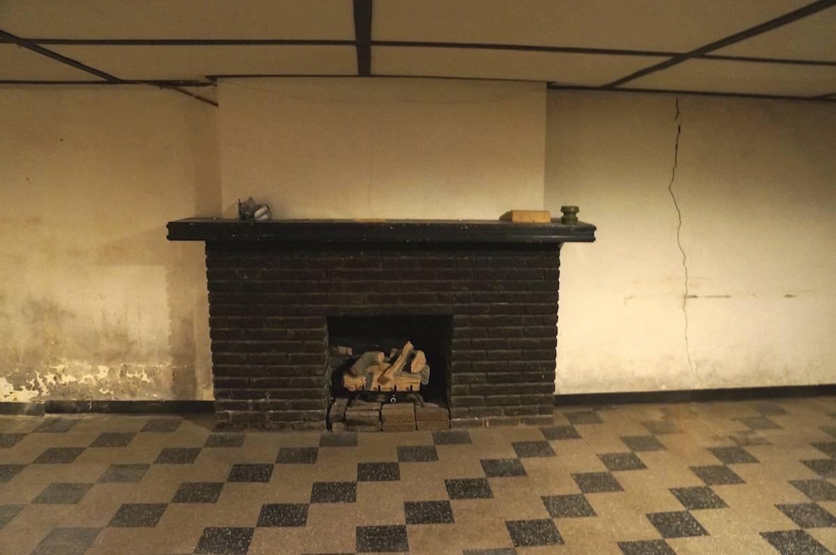 Dark brick wood-burning fireplace in an empty room with checkerboard flooring.