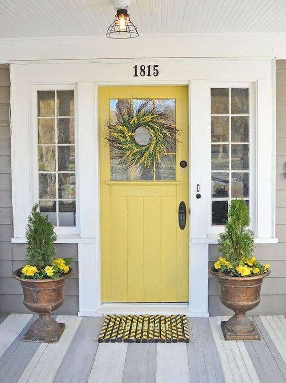 Plants sit on either side of a yellow door with a wreath.