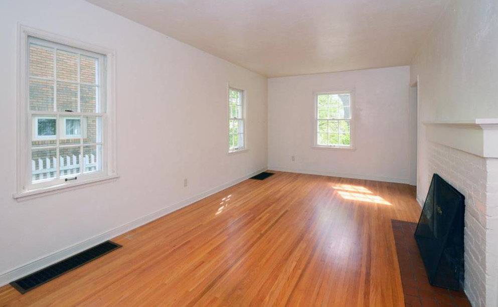 An empty white room with three windows and a wooden floor.