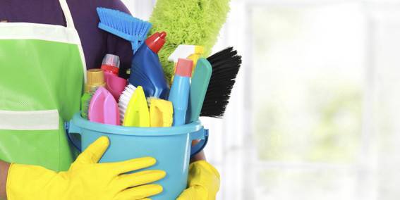 A person with hand gloves is holding cleaning items in a bucket.