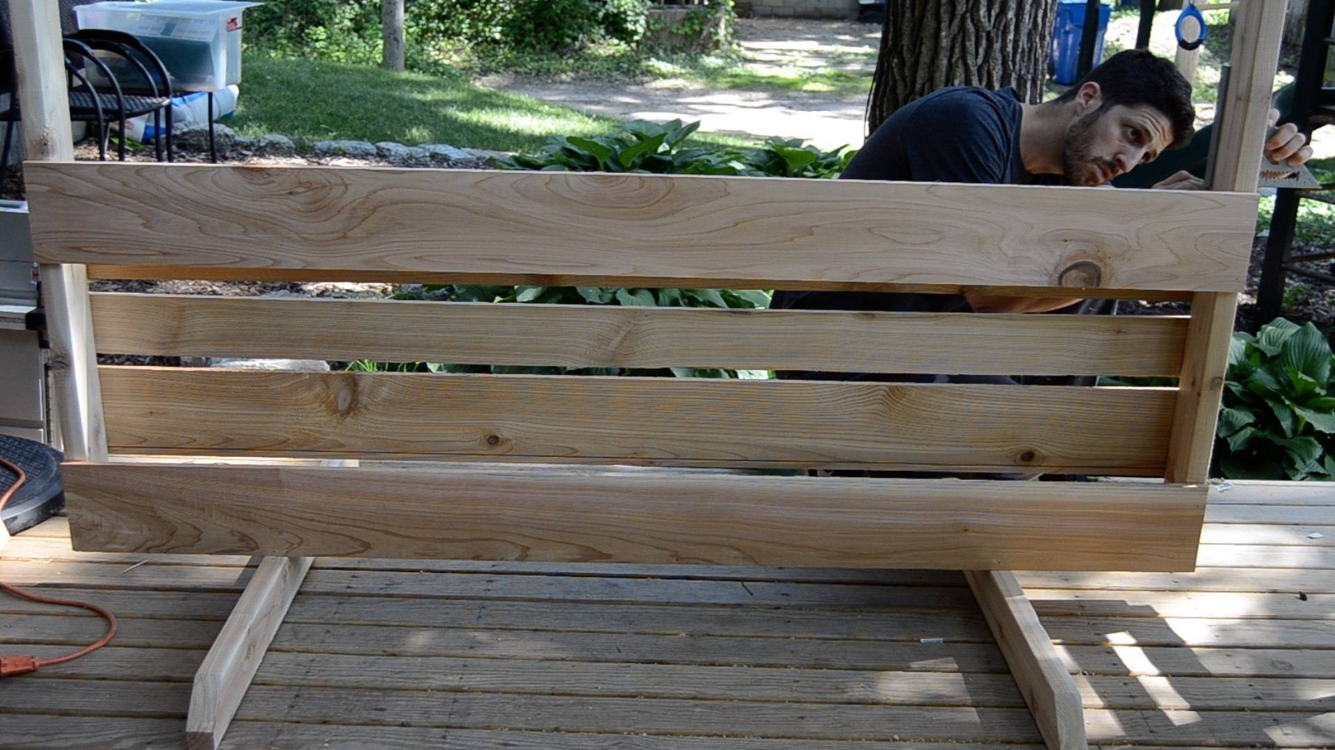 A man is building a wooden plant wall on a deck.