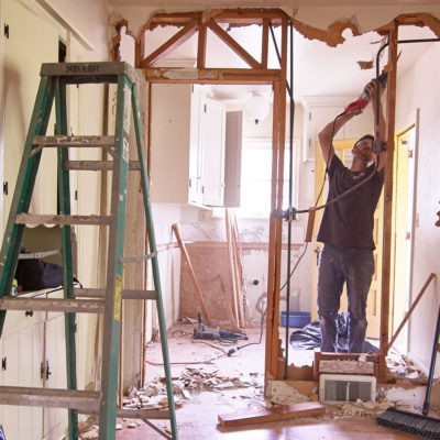 A man uses a tool to remove sections of drywall.