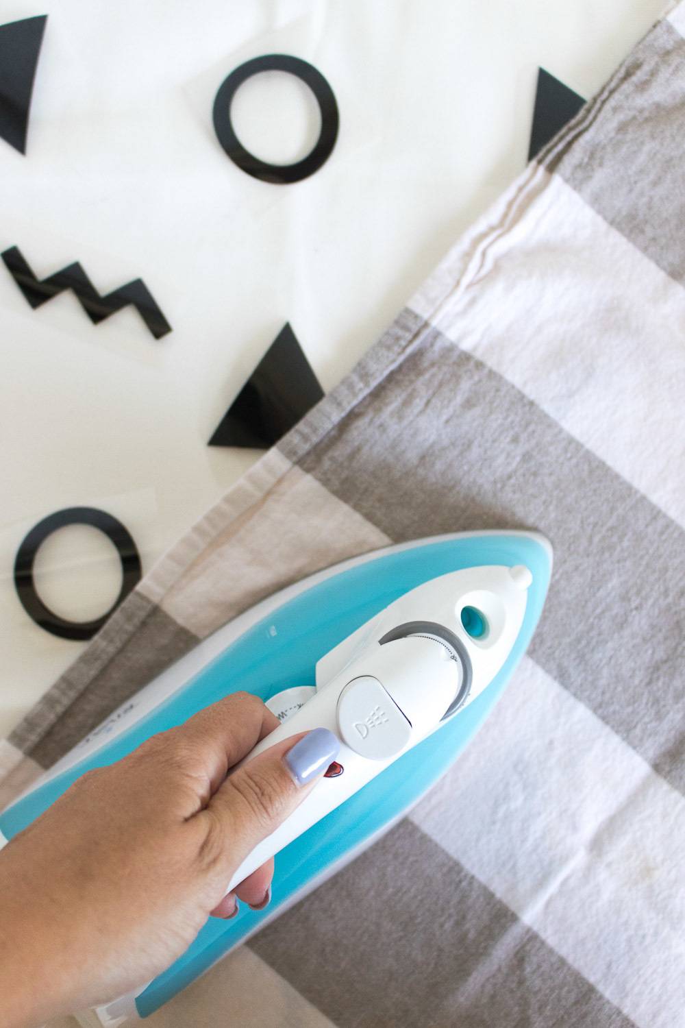A person is using a blue and white iron to iron a piece of clothing.