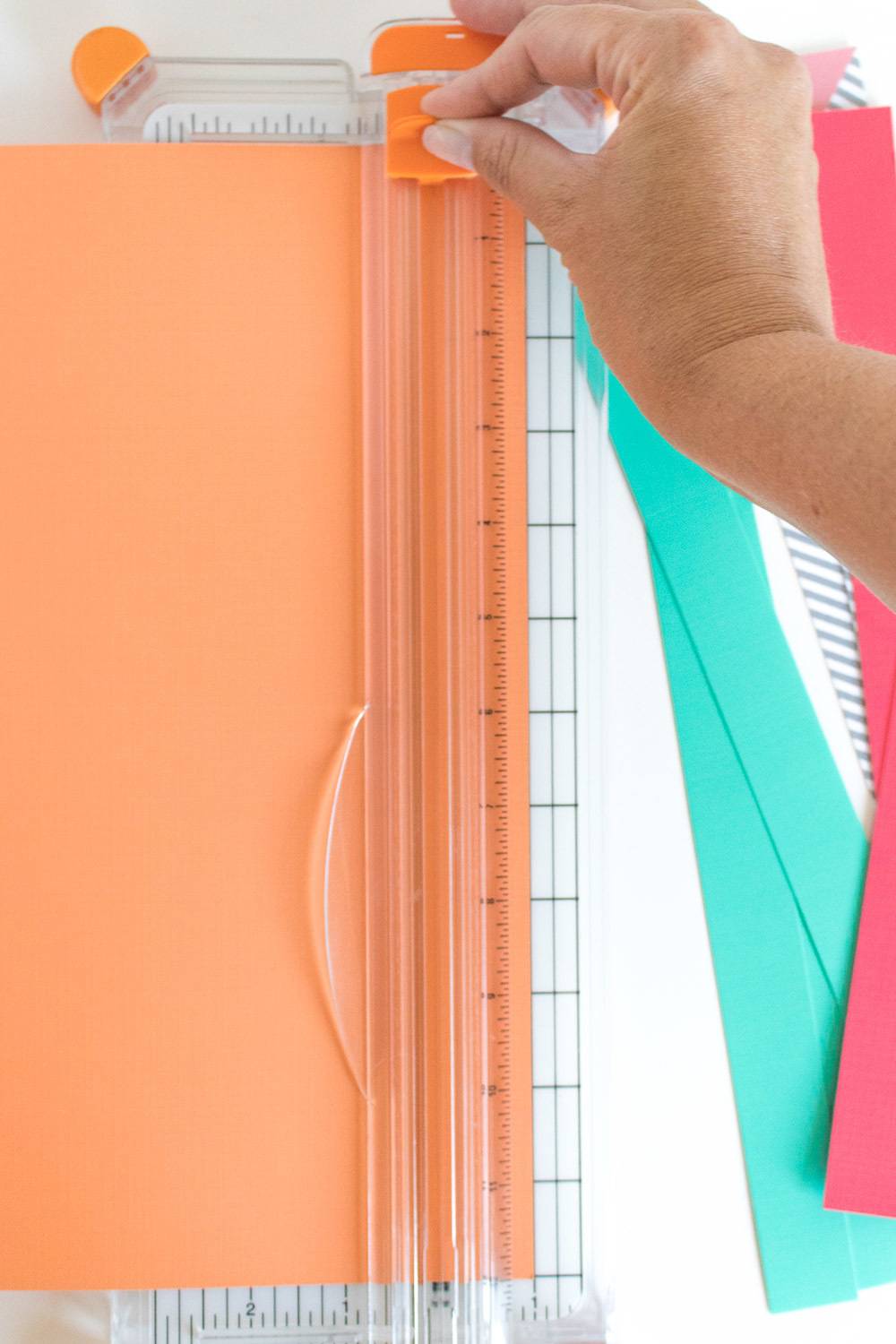 A hand uses a cutting object with orange construction paper in it.