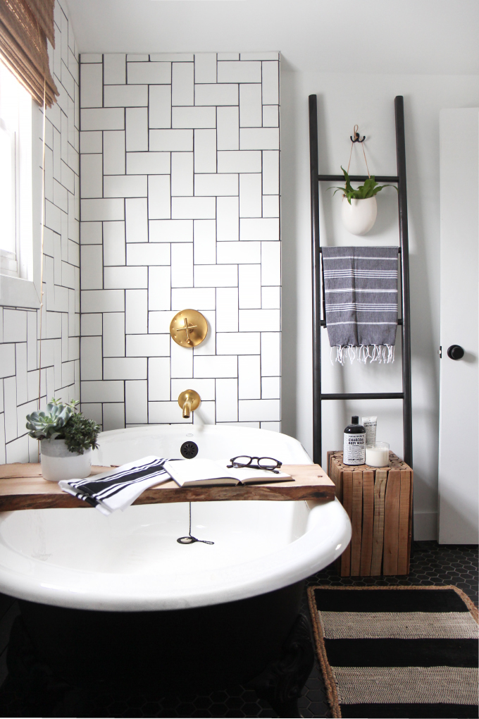 Bathroom featuring a white oval tub with a plank shelf across its top, white subway tile, and a ladder rack.