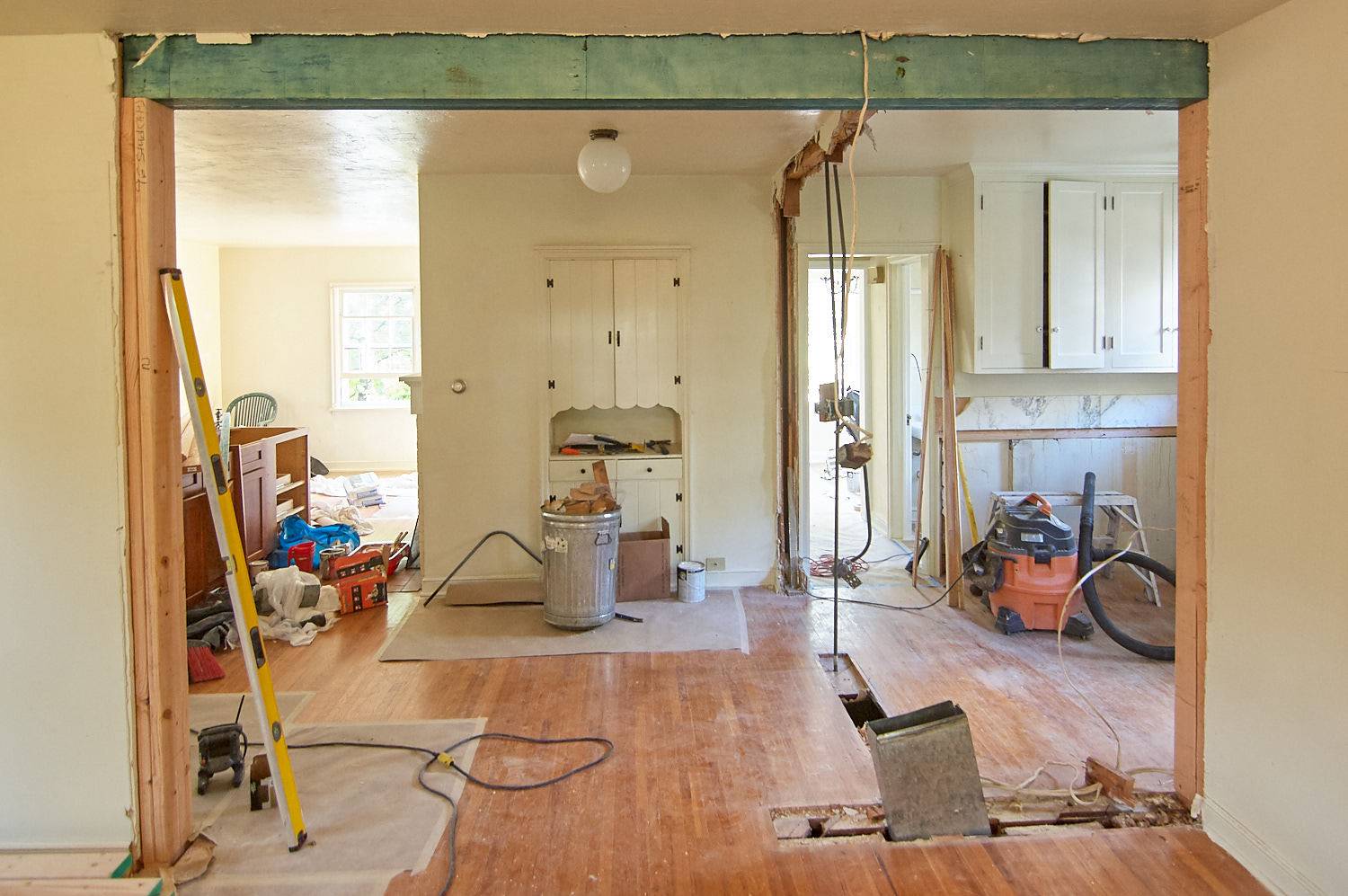 The interior of a house in the remodel stage, with tools laying around and a green support beam across the entryway.