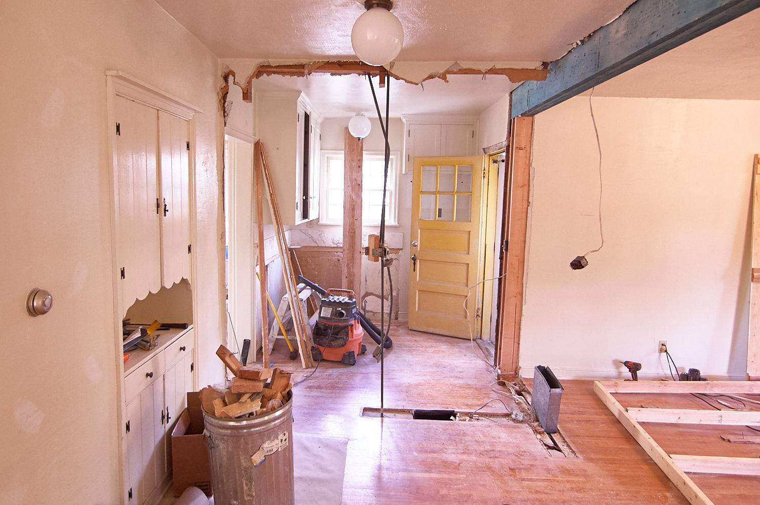 A room under construction with a full silver garbage can of wood pieces.