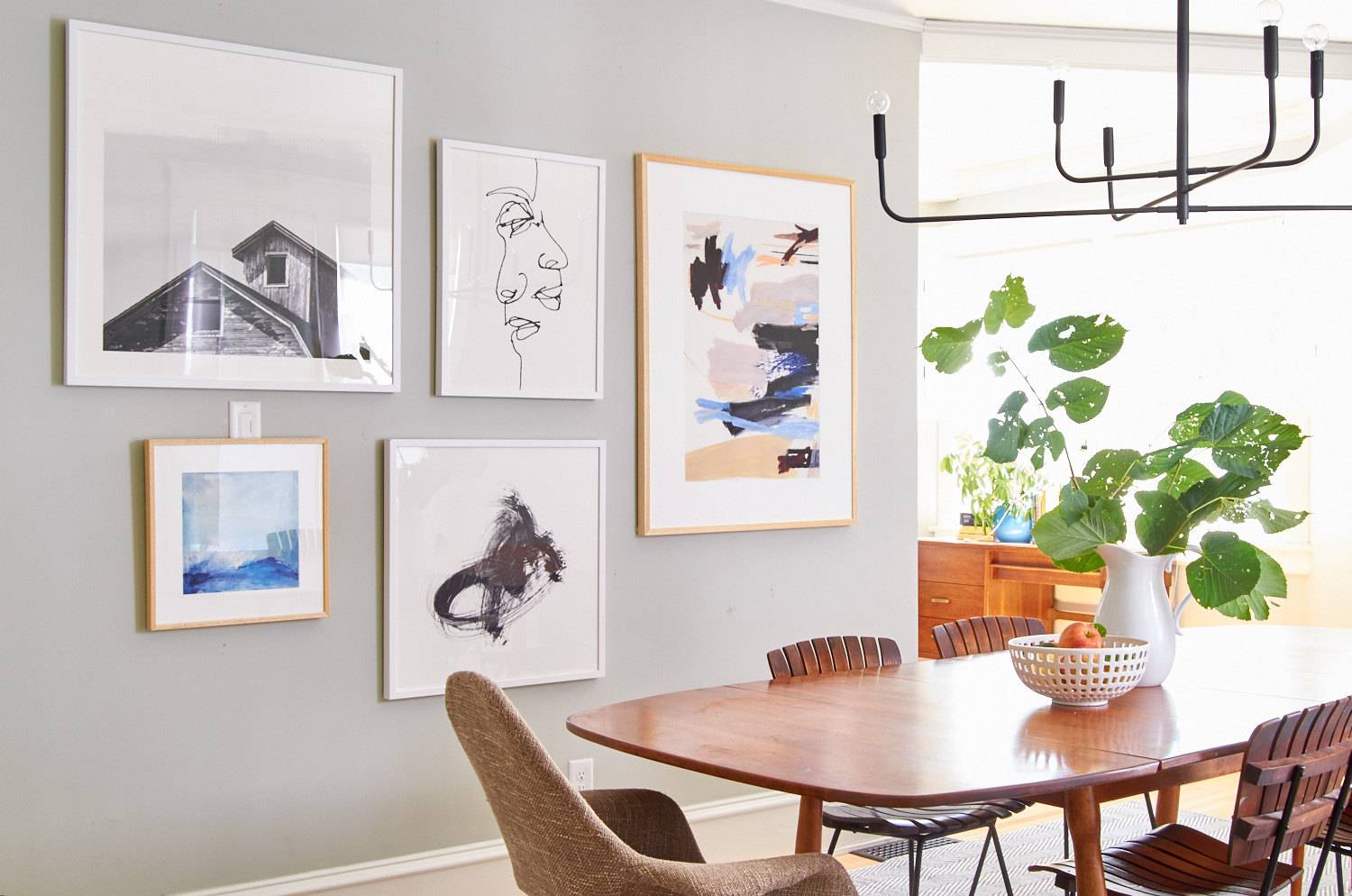 A dining room table with a plant on it sits near a wall with paintings on it.