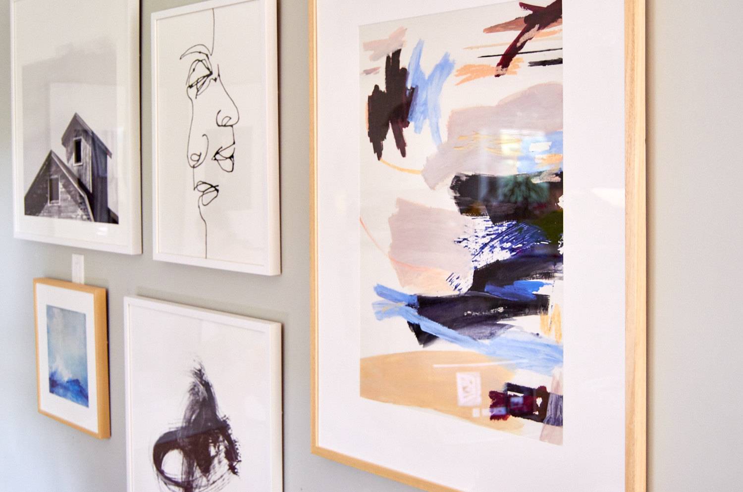 Several modern art paintings in frames are hanging on a wall.