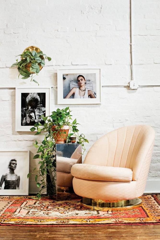 A yellow chair is on a rug in a white room with pictures displayed.
