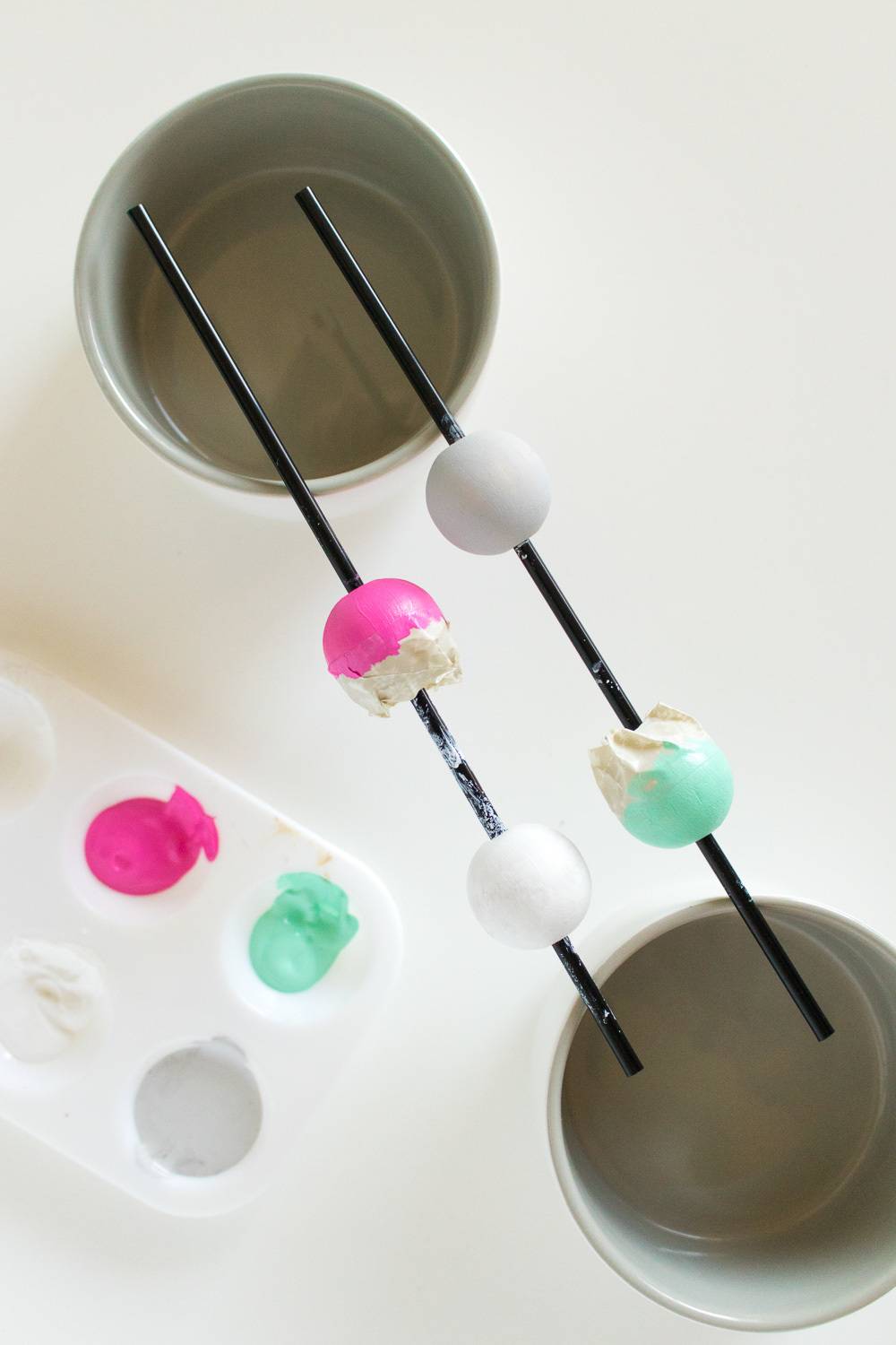 Two black sticks with colored balls on them suspended between two white cups.