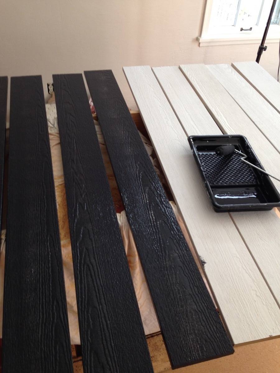 A tray full of black paint and a roller are sitting on half-painted wooden boards.