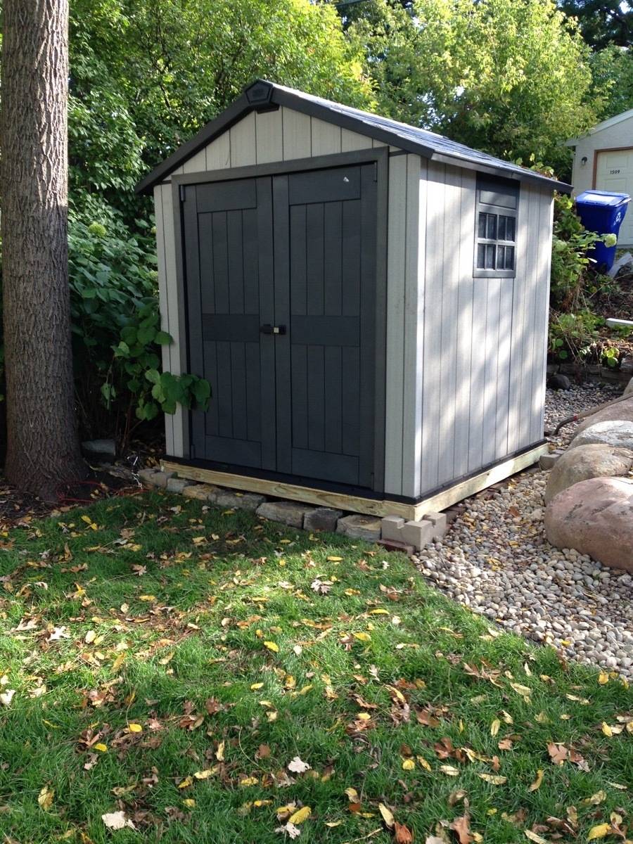 A small backyard tool shed with light colored walls and a set of dark double doors.