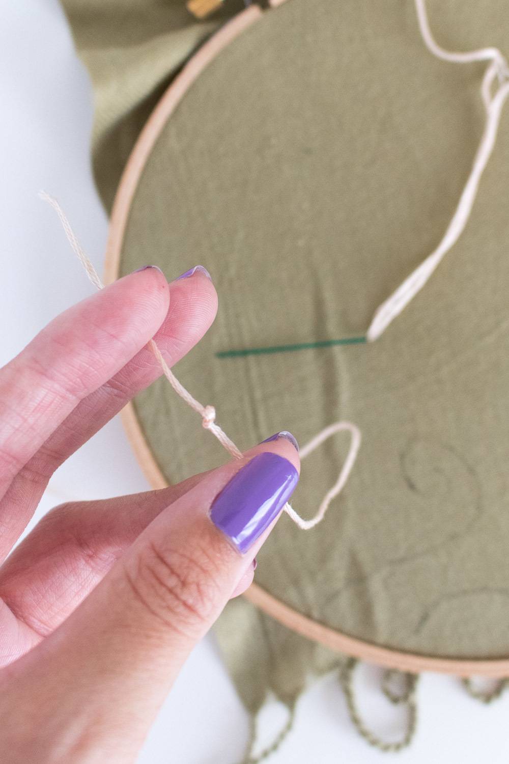 A woman's hand holding a loop while doing some sort of needlecraft.