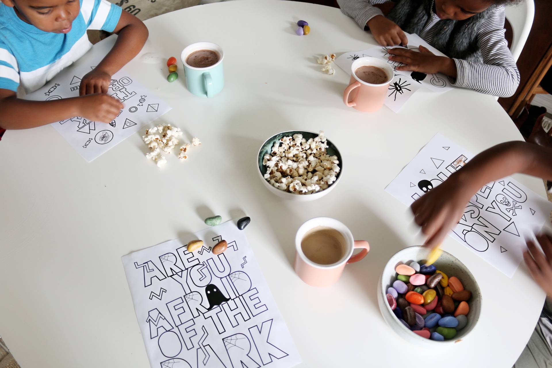 A large white table with chocolate milk, popcorn, and three children coloring