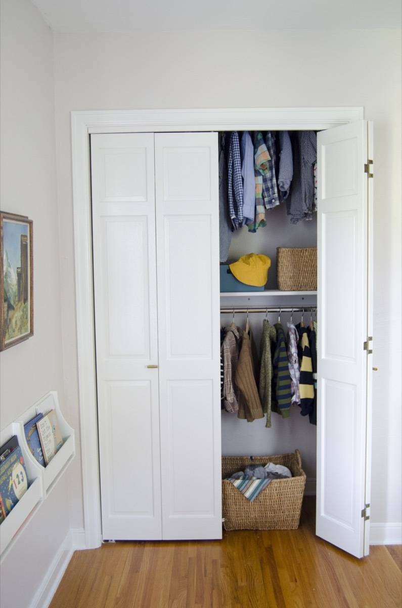 Small home closet with an open door showing hung up clothes and accessories for a small boy.