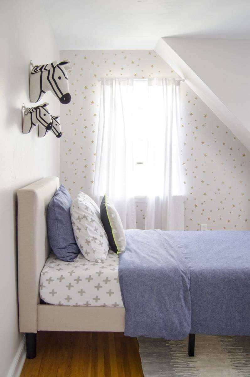 Young boy's bedroom with a small bed with a blue comforter sitting up against a white wall where horse figures are hanging.