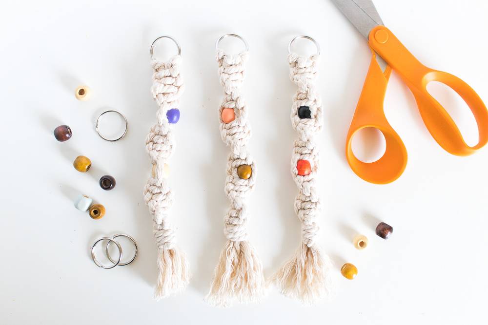 Twisted macrame keychains sitting on a white table next to a pair of scissors with an orange handle.