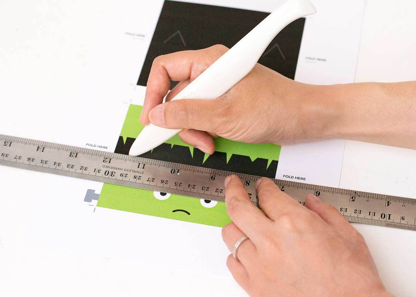 A person cutting a green and black craft project with a white cutter and a silver ruler.