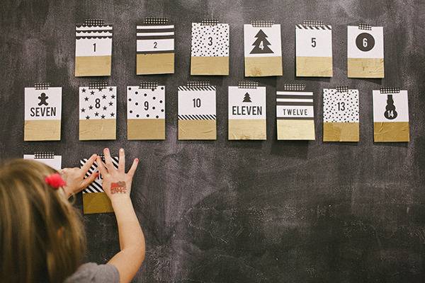 A girl puts up gold white and black pages on a wall to create an advent calendar.