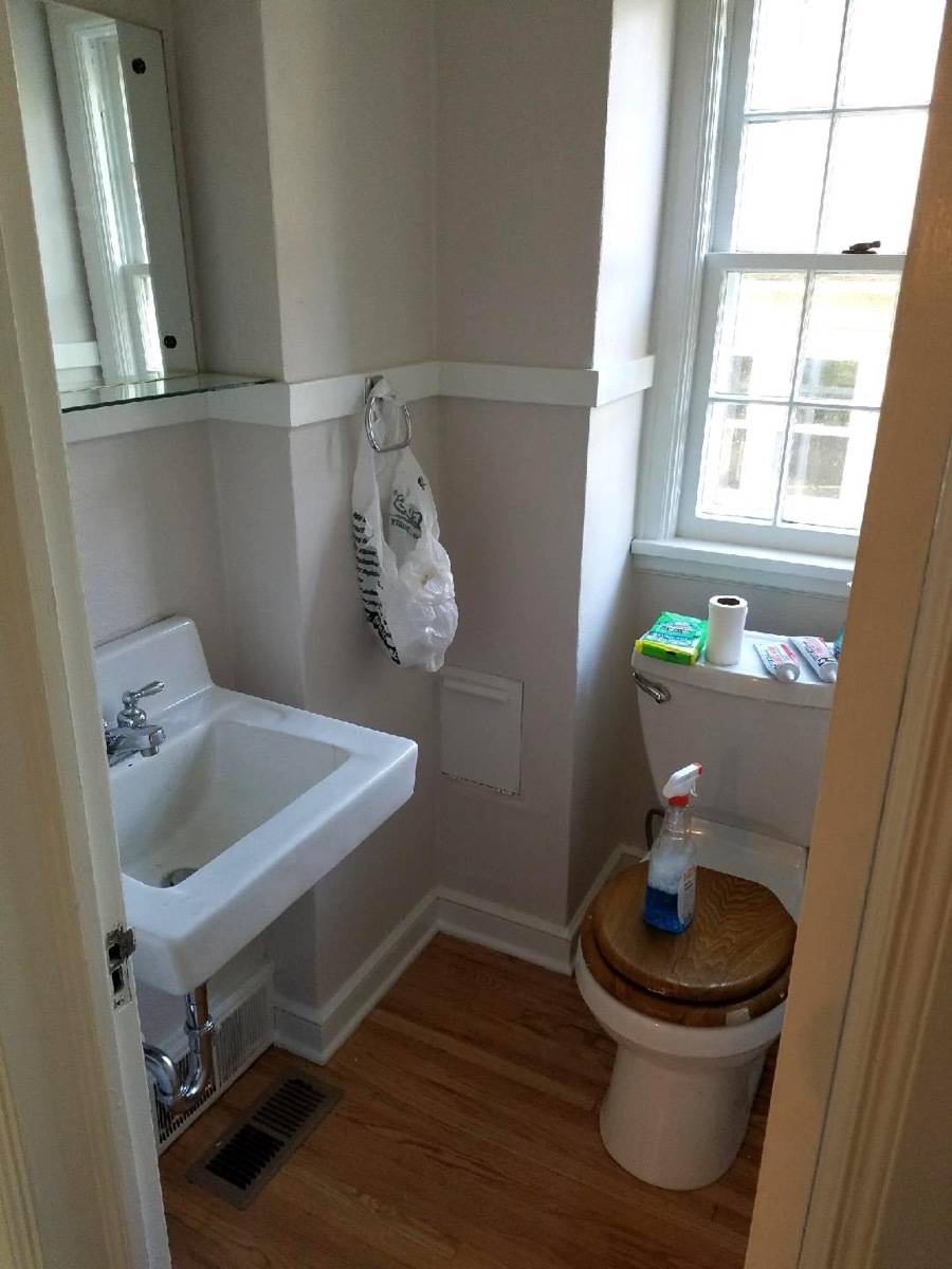Tiny home bathroom with wood trim on the toilet seat and small mirror on the wall.