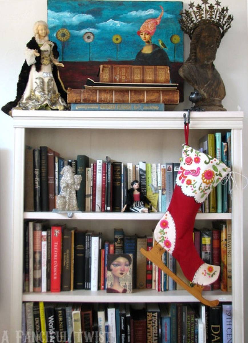 Books sit on a shelf with a stocking hanging from it.