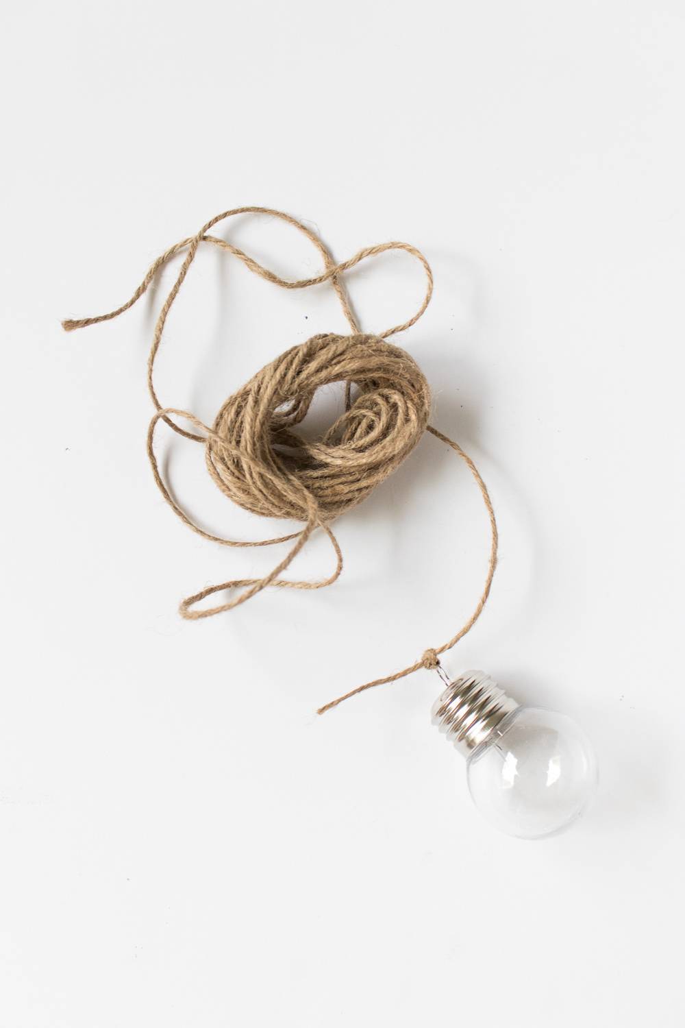 A small ball of brown twine sits on a table next to a small lightbulb.