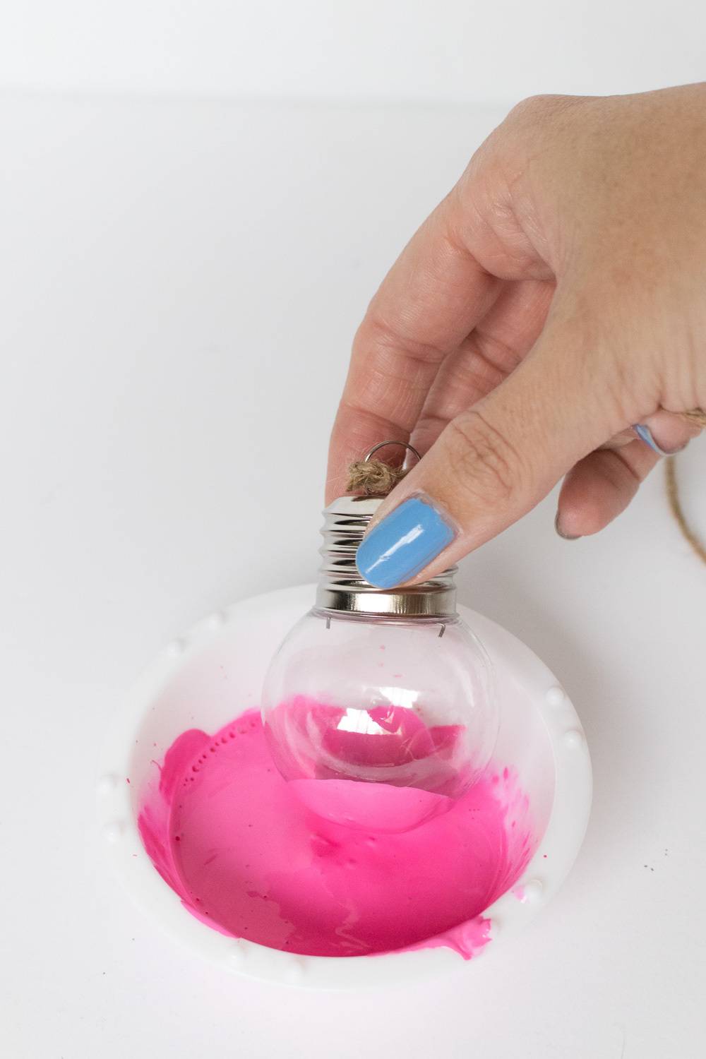A person with blue nail polish holding an ornament with pink fluid in it.