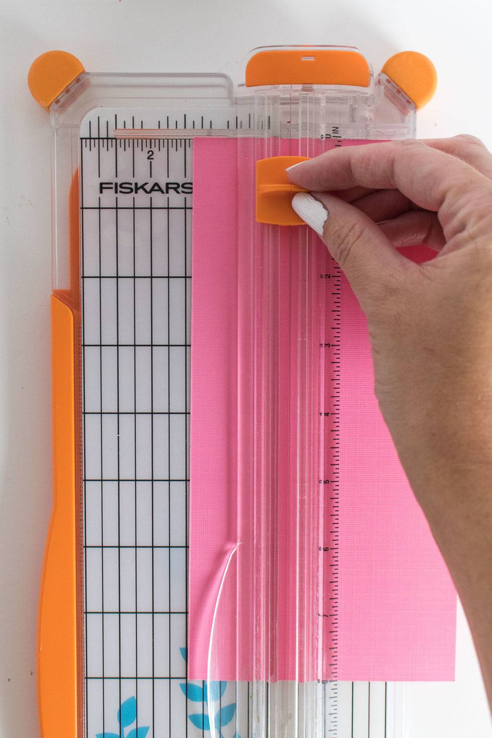 Woman using a paper cutter to cut a hot pink sheet of paper.