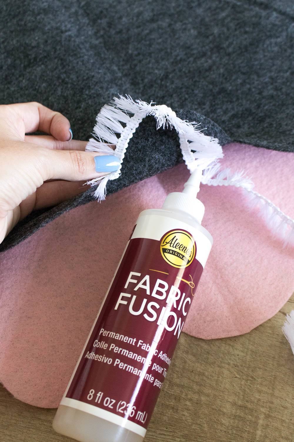 A person is gluing White Fringe on to Pink fabric using fabric glue.