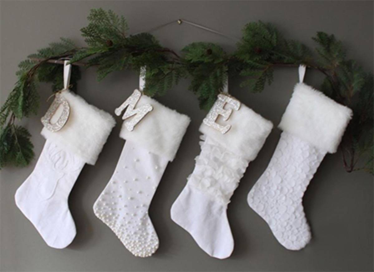 Four white Christmas stockings hang under a string of plants.