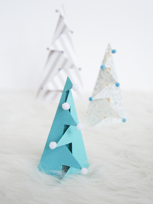 A blue paper tree with white ball tips, a grey and white striped paper tree and a grey paper tree with blue ball tips.
