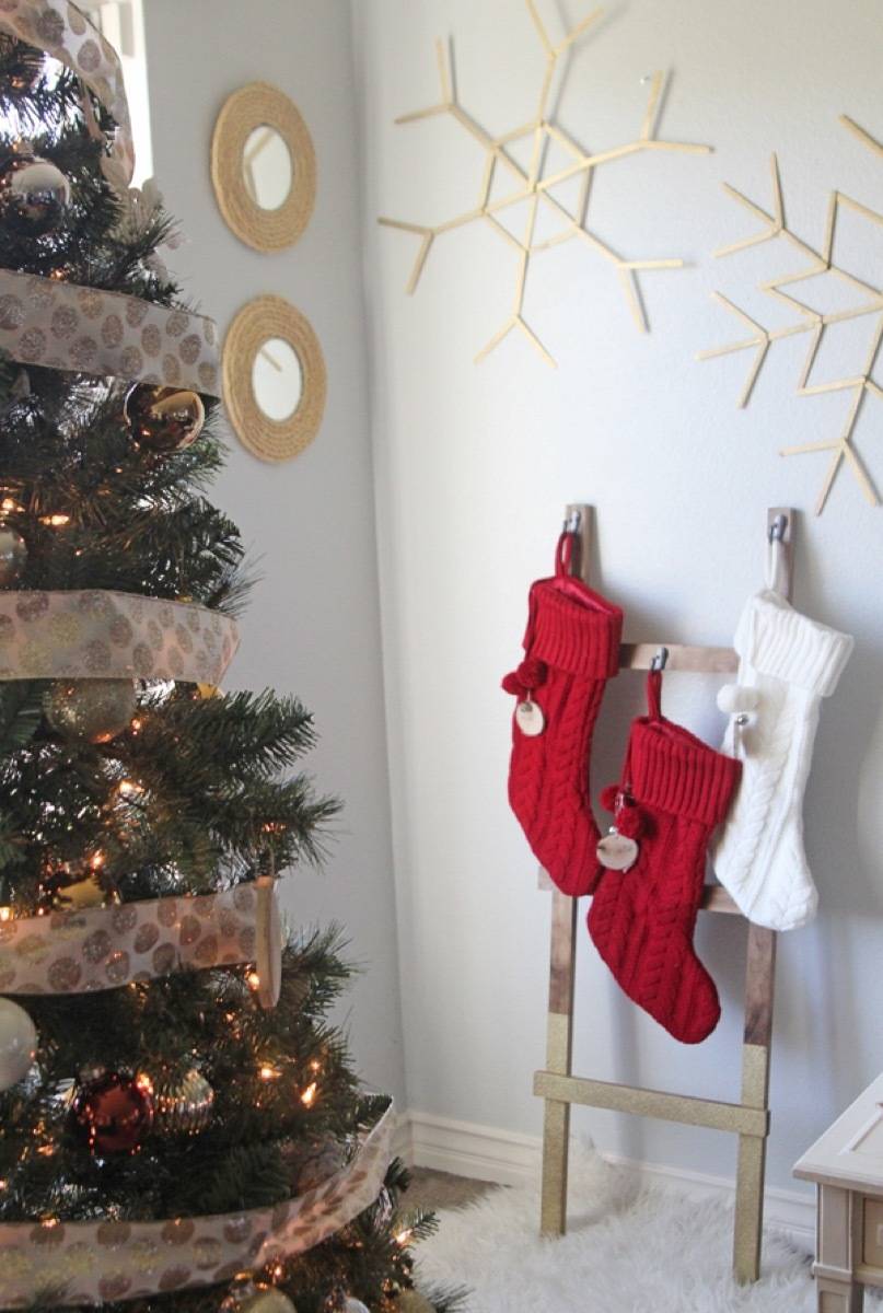 Red and white stockings hang near a white wall near a Christmas tree.