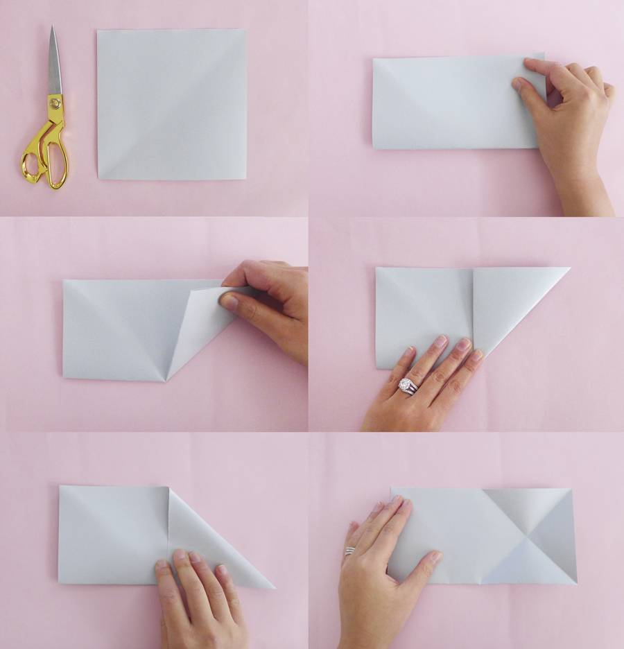 A person is folding a sheet of white paper on a pink surface.