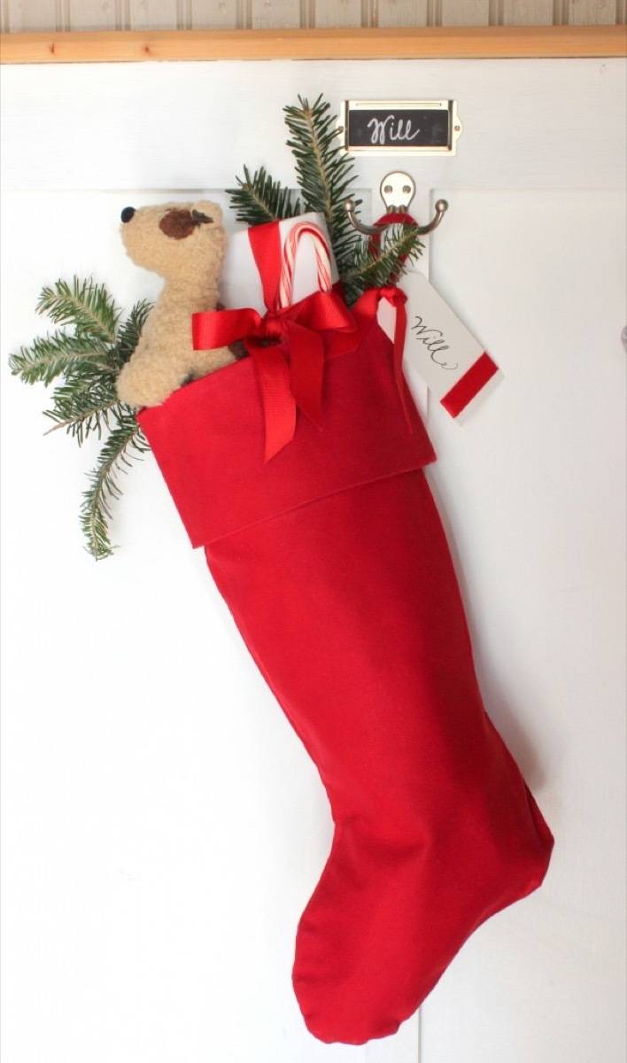 A red stocking hanging with a toy dog, a present and some greenery showing out the opening.