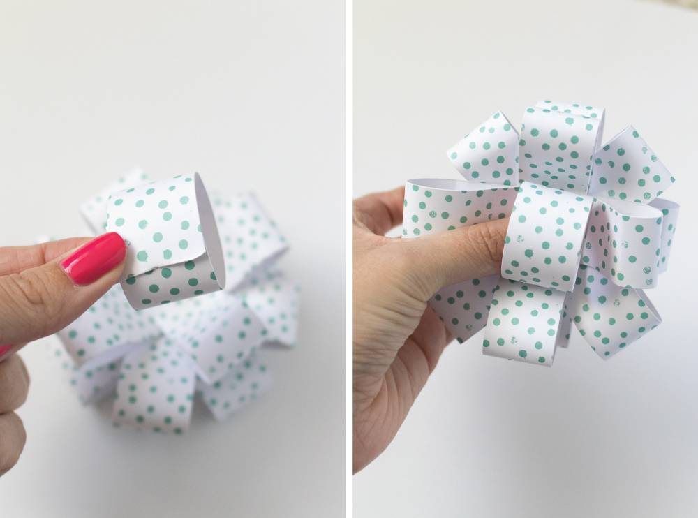 A woman glues together white paper with teal polka dots and rolled into circles to make bows.