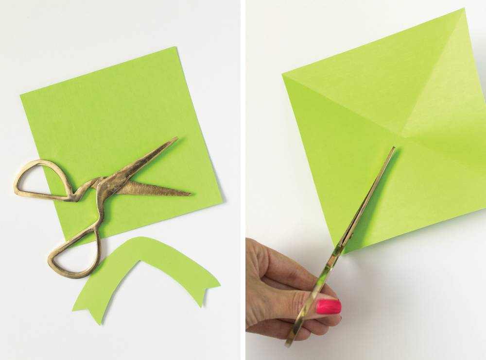 A person using scissors to cut some green paper.